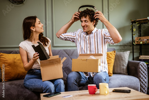 Adult couple is unboxing their packages delivered to home address. They are showing new products to each other.