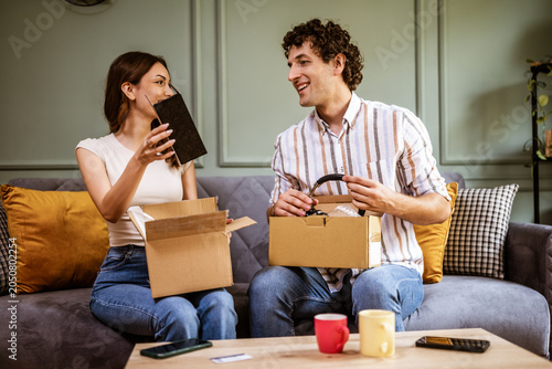 Adult couple is unboxing their packages delivered to home address. They are showing new products to each other.