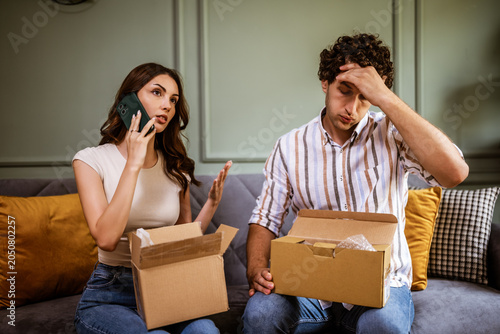 A young couple at home, visibly upset while unpacking a delivery. The man and woman examine the box with displeasure, expressing frustration over a mistake with their home delivery.