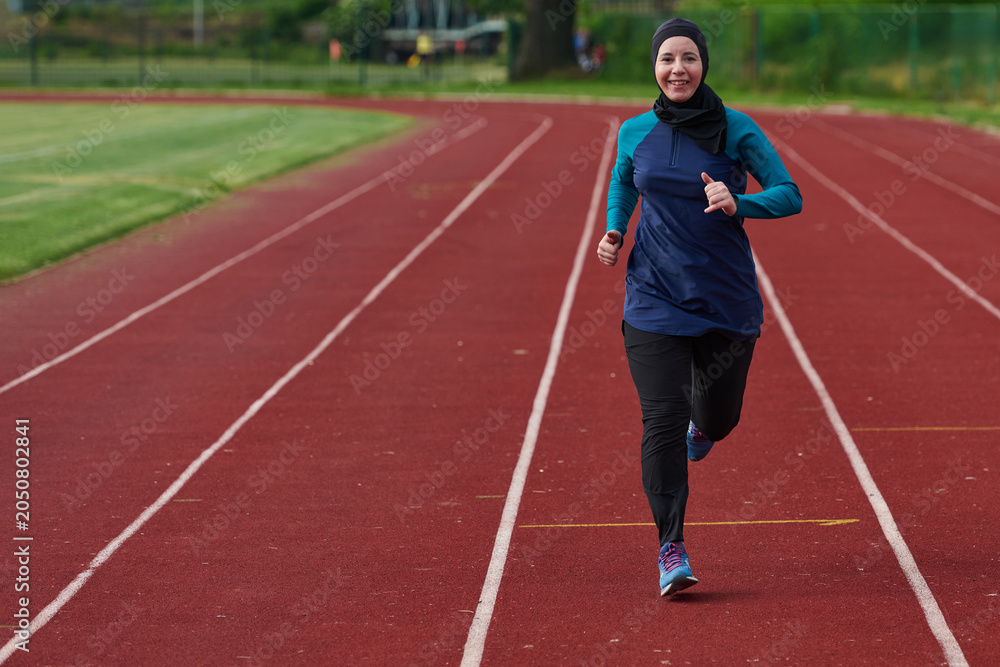 Obraz premium Smiling Female Runner Wearing Headscarf Jogging On Outdoor Track For Fitness And Health