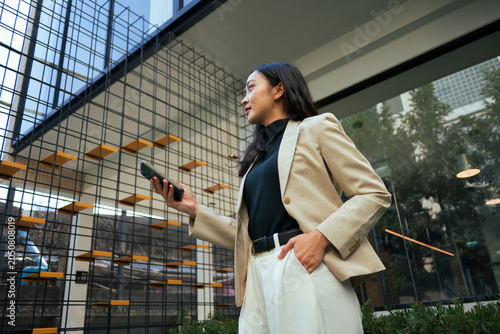 Photos Young businesswoman holding smartphone in modern urban environment