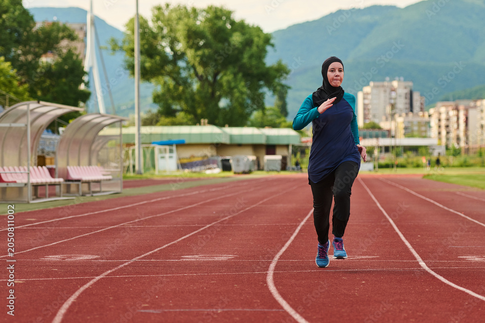 Fototapeta premium Female Runner Wearing Hijab Sprinting on Outdoor Track for Fitness and Athletic Training