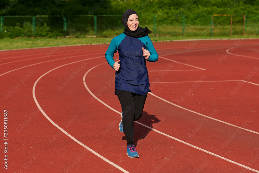 Obraz premium Muslim Woman Running on Outdoor Track in Sports Hijab Practicing Fitness and Jogging