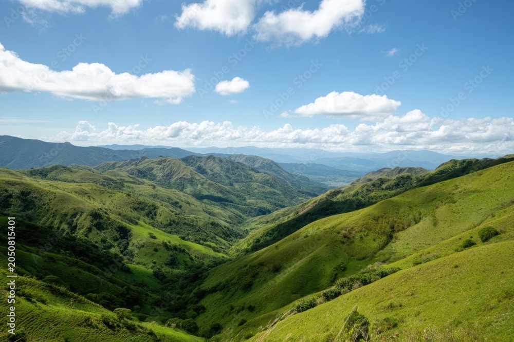 Fototapeta premium The hills rolling into a green valley beneath a bright blue sky with clouds