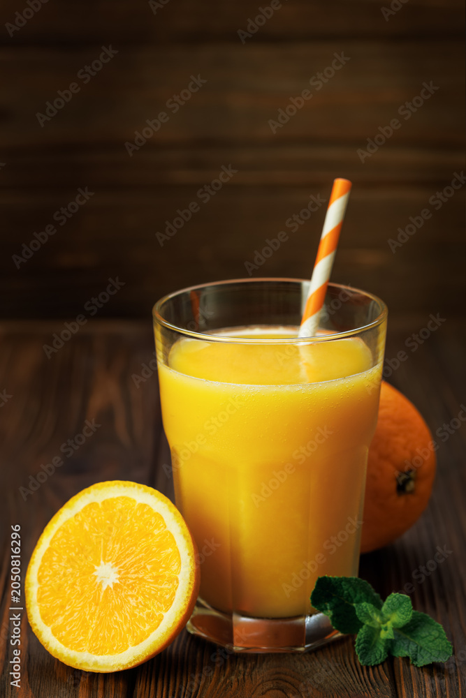Fototapeta premium Glass of freshly squeezed orange juice with striped straw, mint and citrus fruits on rustic wooden background