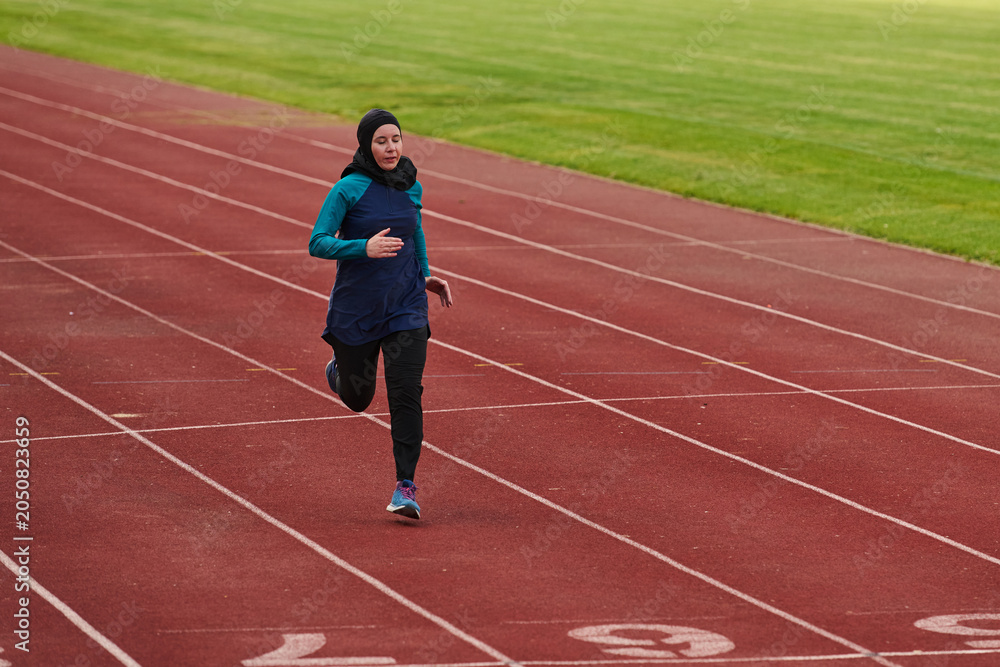 Fototapeta premium Female Athlete in Headscarf Running on Outdoor Track During Sprint Training Session