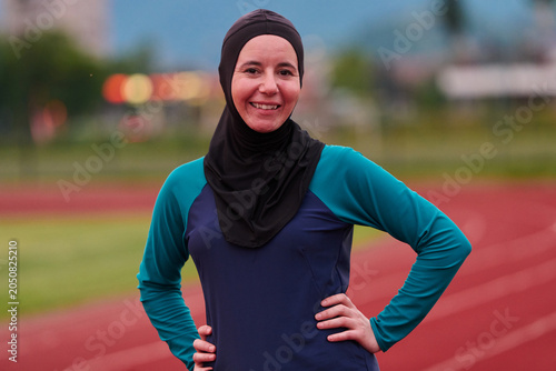 Bild auf Leinwand Smiling Female Athlete in Sports Hijab Posing on Outdoor Running Track at Dusk