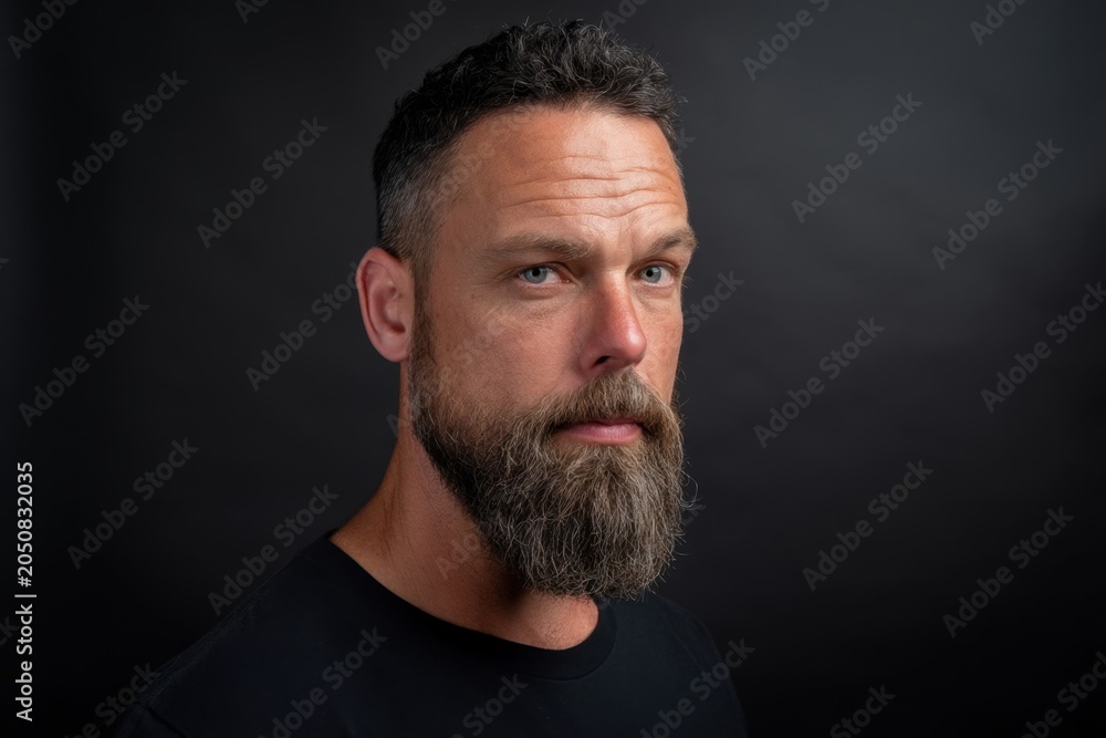 Fototapeta premium The bearded man in a moody studio portrait with intense blue eyes and serious expression
