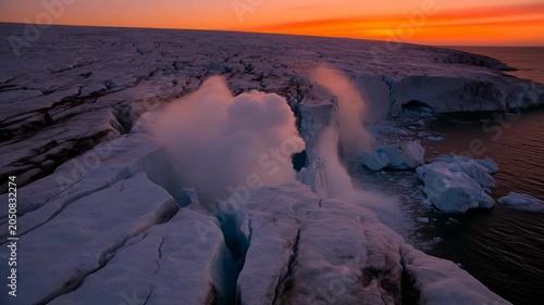 Collapsing coastal ice shelf sending spray and icebergs into ocean at sunset as crevasse widening