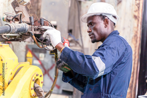 Konstfotografi Closeup a black man foreman inspects automated robotic arm welding machine for repair in the automotive industry's maintenance department