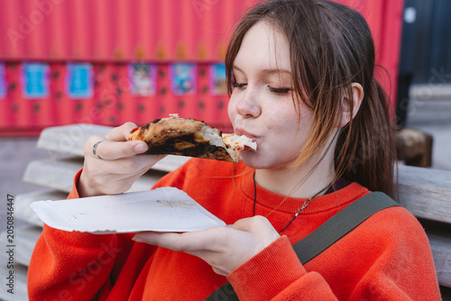 Person eating pizza outdoors wearing an orange sweater