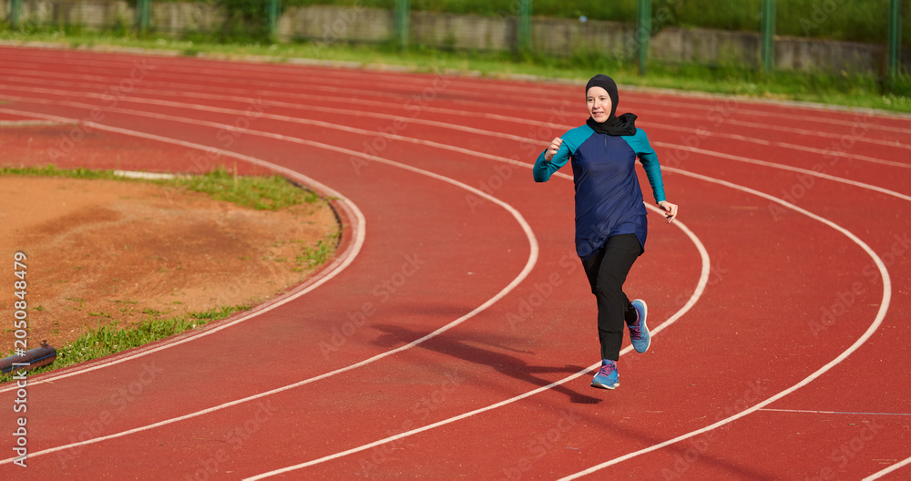 Fototapeta premium Young Muslim Woman Running on Outdoor Track in Hijab Training for Fitness and Athletics