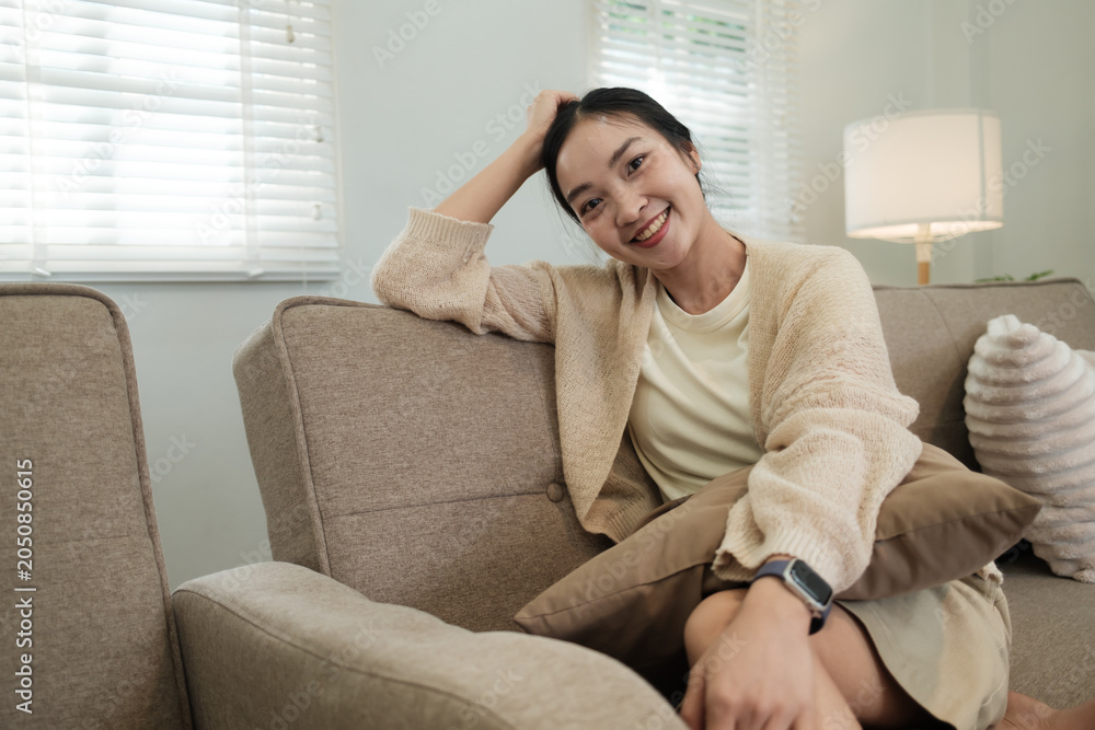 Fototapeta premium Young Asian woman smiling broadly relaxing on sofa at home