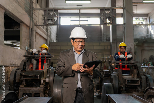 Senior Asian industrial engineer using digital tablet to inspect factory production line background.