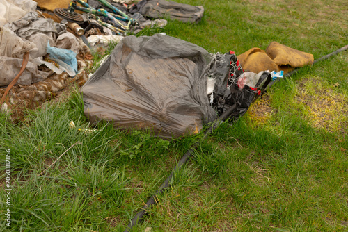 A pile of outdoor equipment and protective gloves left on a grassy field. A grey tarpaulin partially covers tangled ropes, metal poles, and fabric bundles