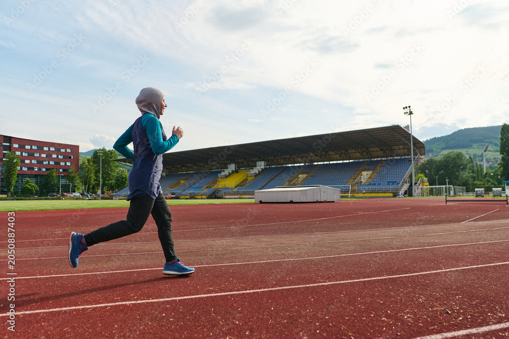 Fototapeta premium Young Woman in Hijab Running on Outdoor Track Beside Empty Stadium for Fitness Training