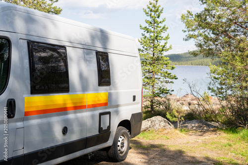 Campervan parked by lakeshore in pine forest during summer road trip in Finland