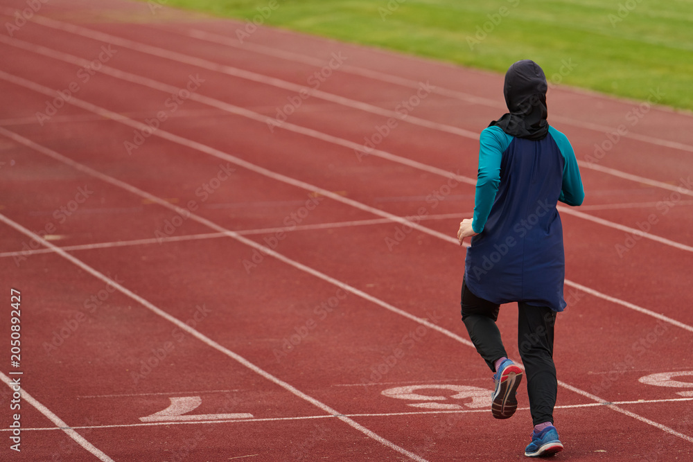 Obraz premium Female Athlete Running on Outdoor Track Wearing Headscarf Training for Fitness and Endurance