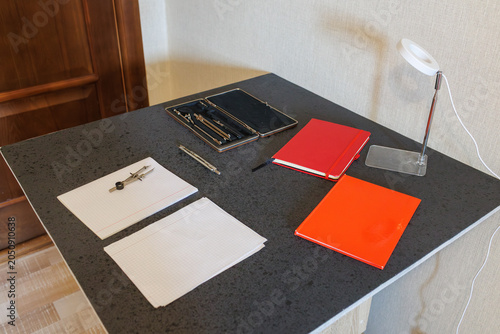 Desk with notebooks, drafting set, paper and lamp, high-angle side view with door in background