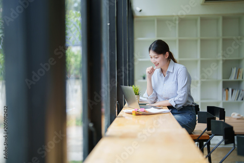 Fotografie Young asian businesswoman smiling, enjoying laptop work at a co-working space, m