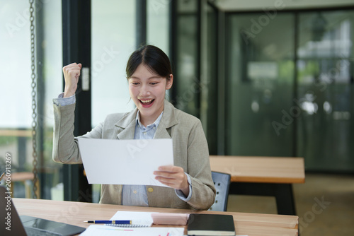 Foto Happy young asian business woman celebrating great news, reading document with s