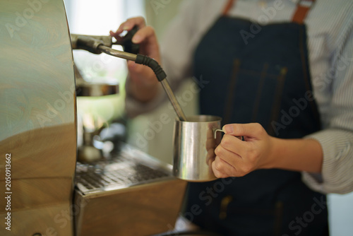 Foto Barista preparing specialty coffee beverages, steaming milk in a stainless steel
