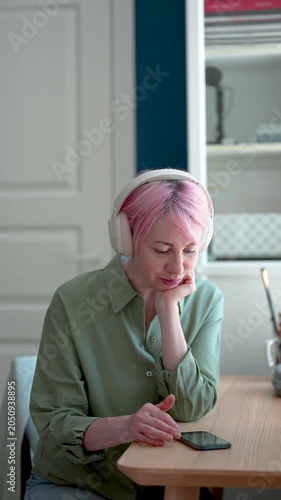 Relaxed positive mature woman reading blog feeds online on smartphone and listening music, tranquil smiling female in headphones enjoying favorite playlist, browsing social media online on cellphone