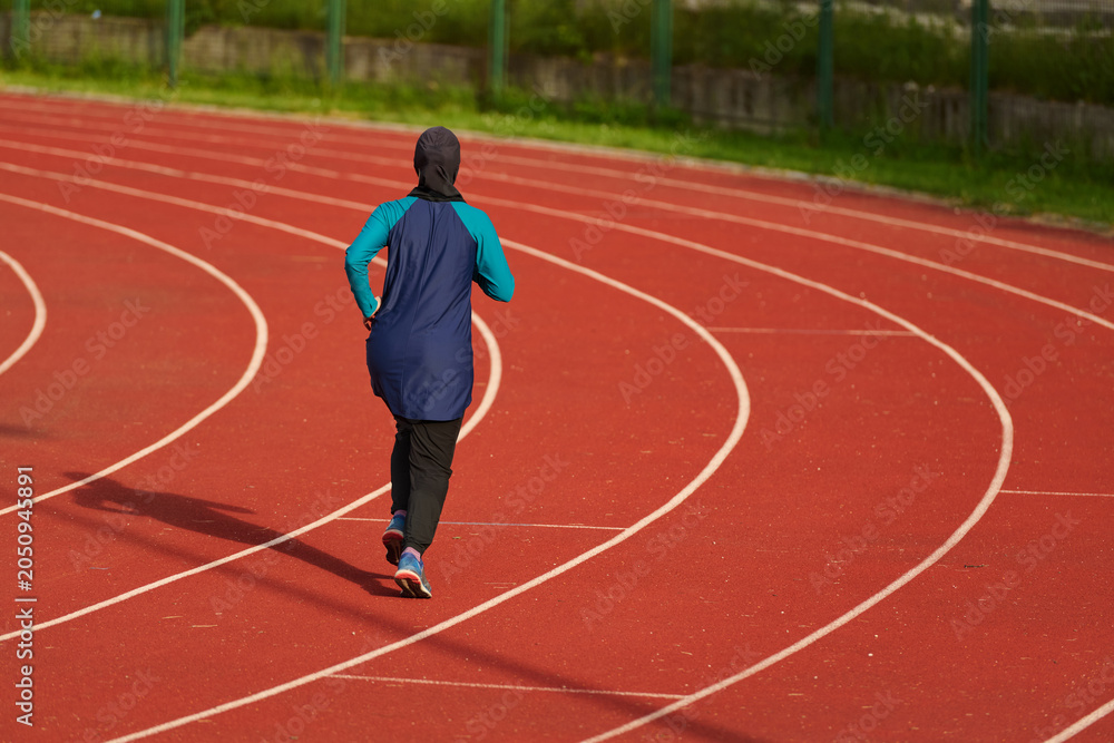 Fototapeta premium Female Runner In Hijab Jogging on Outdoor Red Track Lane for Fitness Training and Endurance