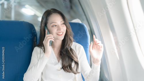 Bilde på lerret An Asian businesswoman happily uses her smartphone while traveling on an airplane
