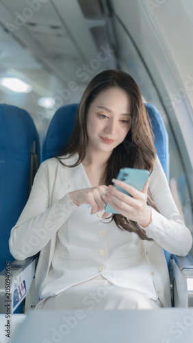 Fotografia An Asian businesswoman happily uses her smartphone while traveling on an airplane