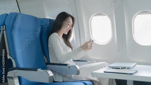 Фотография An Asian businesswoman happily uses her smartphone while traveling on an airplane
