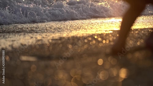 Low angle perspective of boy girl walking on wet sandy beach. Ocean waves gently wash shore. Golden hour sun creates sparkling bokeh reflections on water and wet sand. Peaceful and serene atmosphere. 