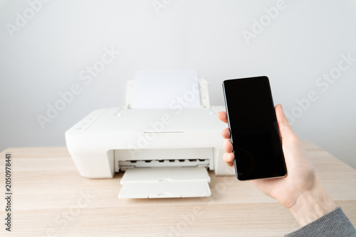 Person Holding Smartphone in Front of Printer for Wireless Mobile Printing in Home Office