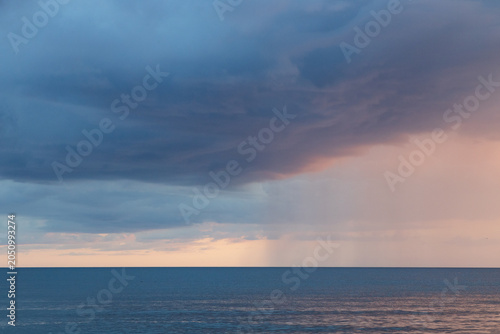 Dramatic Ocean Storm With Rain Shaft and Pastel Sunset Clouds Over Calm Horizon