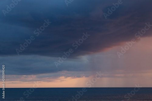 Dramatic Ocean Storm With Rain Shaft and Pastel Sunset Clouds Over Calm Horizon
