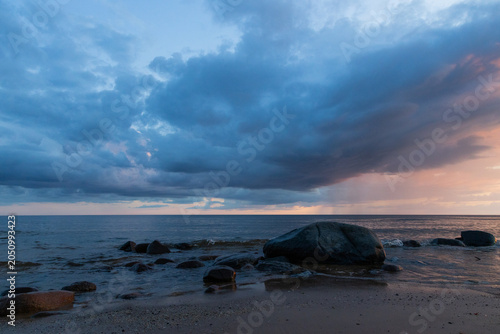 Stormy Sunset Over a Rocky Beach With Dramatic Clouds and Calm Sea Horizon