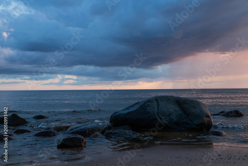 Dramatic Storm Over Ocean At Sunset With Rocky Shoreline And Rainfall On Horizon