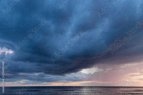 Dramatic Ocean Storm With Rain Shaft and Pastel Sunset Clouds Over Calm Horizon