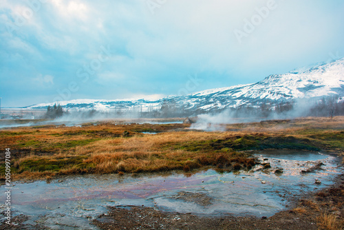 Steaming geothermal hot springs in Haukadalur valley with snowy mountains in Iceland. High quality photo