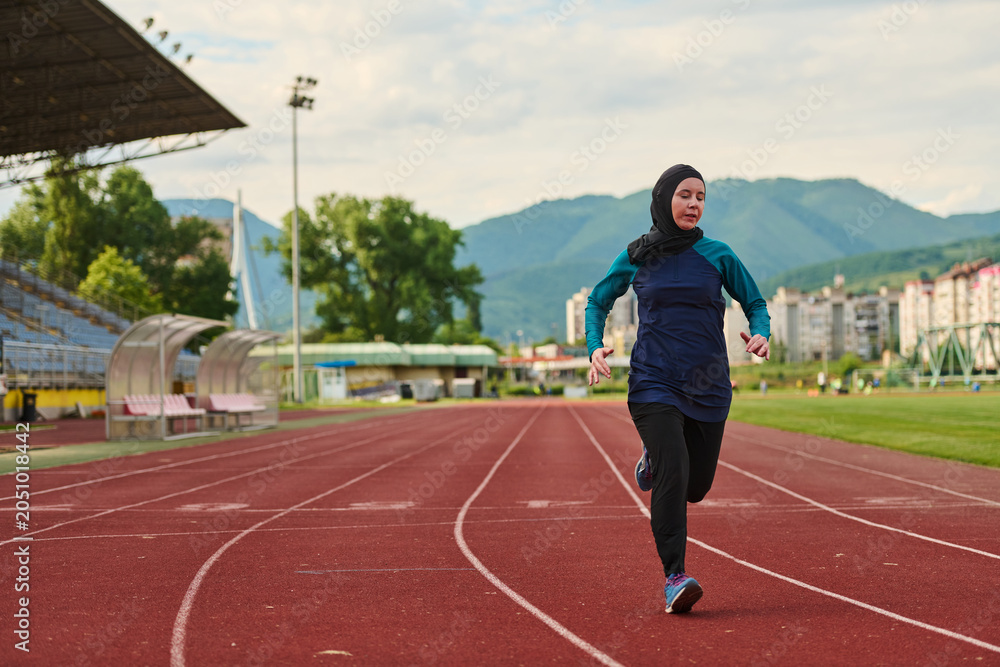 Obraz premium Woman in Hijab Running on Outdoor Track at Stadium Training for Fitness and Athletics
