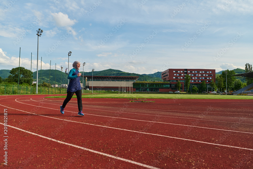 Fototapeta premium Young Woman Running on Outdoor Track Wearing Hijab and Sportswear for Fitness and Training