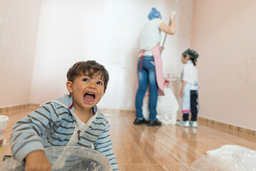 Mother and her children painting home room. Funny boy dirty looking at camera