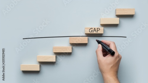 Hand drawing a line across wooden blocks spelling 'GAP' on a grey background