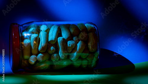 Fotografie Tarro de cristal tumbado con fondo lila y verde con palitos de pan o picos dentro, luces y sombras