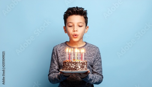 Young boy blowing out candles on a chocolate birthday cake against a blue background