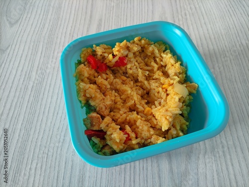 Blue plastic container with rice, vegetables and chicken on wooden table, top view