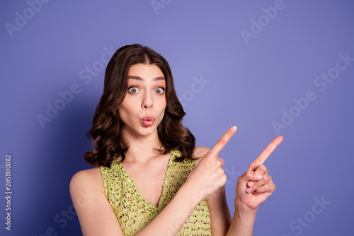 Foto Surprised young woman pointing to the side with puckered lips on purple backgrou