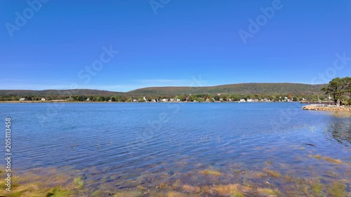 Slow motion footage view across the calm waters of Annapolis Basin in Annapolis Royal Nova Scotia Canada with distant shoreline homes rolling hills and clear blue skies creating a peaceful maritime