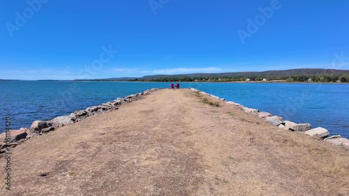 Slow motion footage of scenic rocky breakwater stretching into the waters of Annapolis Basin at Annapolis Royal Nova Scotia Canada with two red chairs at the end of the jetty