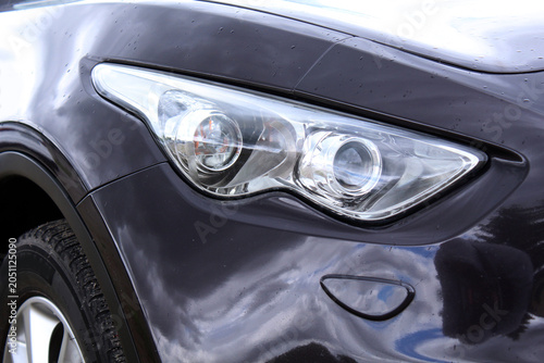 Stylish automobile headlight with projector lenses and polished body panels. Rain droplets on the dark exterior emphasize modern engineering and transportation technology. Modern headlights with dual 